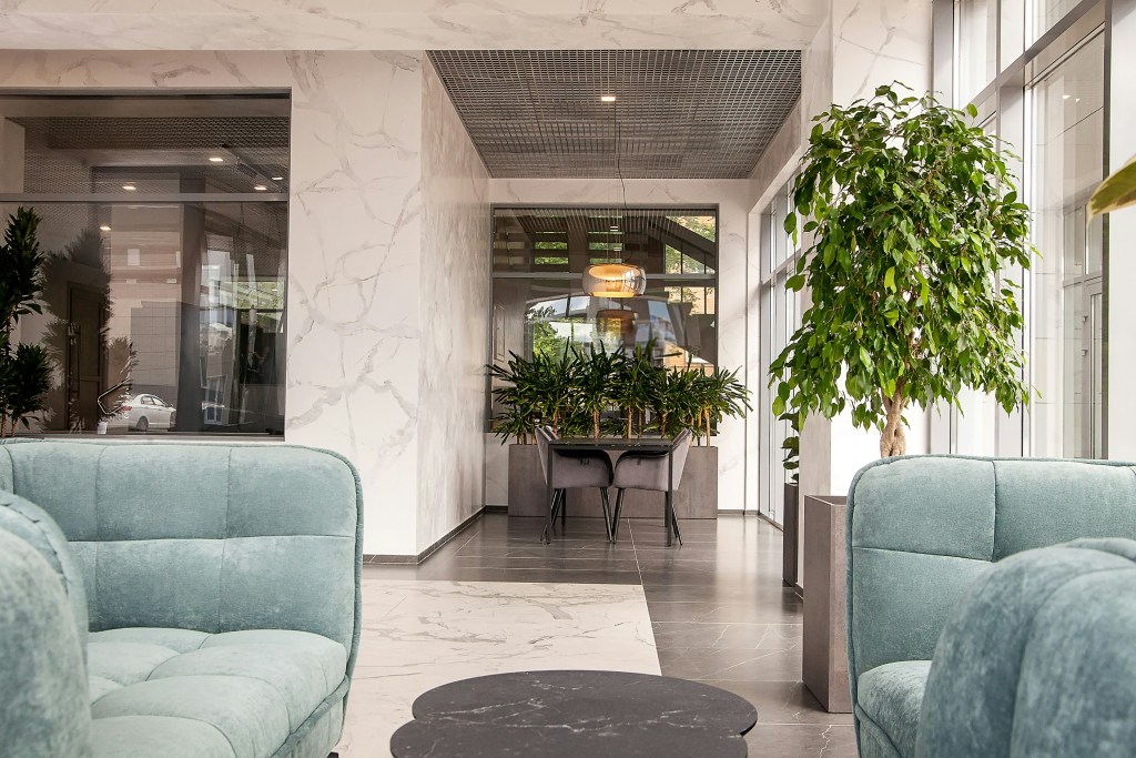 Moderne Lobby mit grünen Sofas, einem runden Tisch und Pflanzen im Hintergrund.